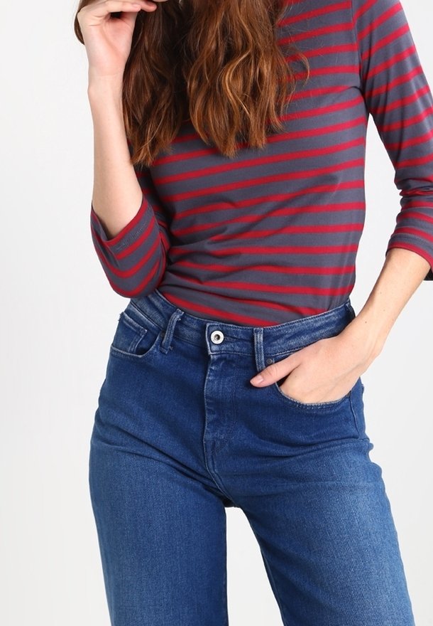 Maglietta a maniche lunghe a righe grigie e rosse abbinata a jeans blu a vita alta. I jeans presentano un bottone frontale e tasche.