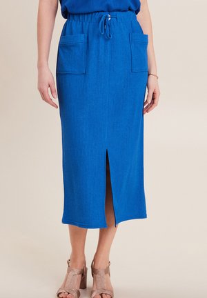 Blauwe geribbelde midi-rok met een koordtaille, voorkantsplit en twee zijzakken. Draagt met beige blokhak sandaaltjes met bandjes.