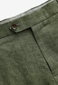 Olive green linen trousers with a front pleat, featuring a button closure and a contrasting checkered lining at the waistband.