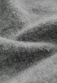 Gray knit fabric with a soft, textured surface, featuring a blend of tightly and loosely woven fibers, creating a varied pattern.
