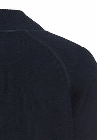 Marineblauwe gebreide trui met een geribbelde kraag en een gladde textuur, met raglanmouwen en subtiele variaties in het breipatroon.