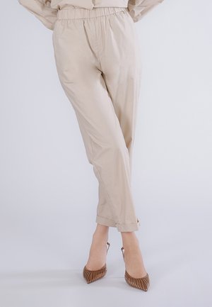 Beige afslappede bukser med høj talje og elastisk linning, opsmøgede ankler, båret med brune slingback-hæle med spids tå.