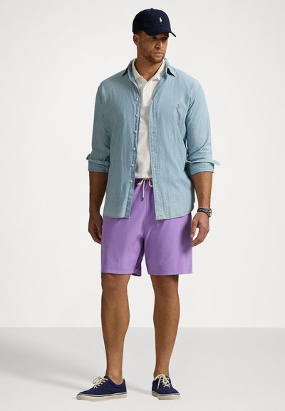 Cămașă din denim bleu deschis, polo alb, pantaloni scurți purpurii și teniși bleumarin. Accesoriile includ o șapcă bleumarin și un ceas.