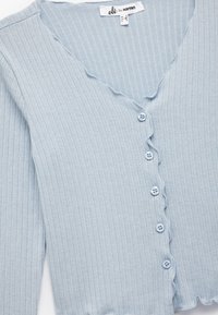 Hellblauer, gerippter Cardigan mit gewellten Kanten, tiefem V-Ausschnitt und sechs blauen Knöpfen vorne.