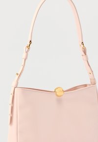 Hele roosa nahast käekott reguleeritava õlarihma ja ümarate kuldsete klambritega, heledal ühtlasel taustal.