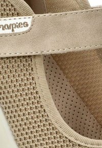 Zapatilla beige con un diseño de malla y acentos de gamuza suave. Forma redondeada con tejido perforado y un borde cosido. Logo visible en la correa.