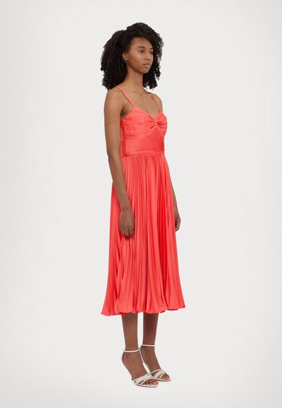 Vestido coral plisado con un bodice ajustado y tirantes finos, que presenta un detalle anudado en la parte delantera y una falda fluida que cae por debajo de la rodilla.