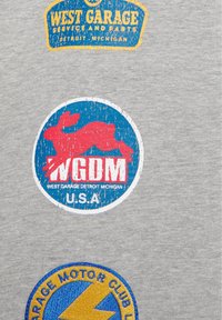 Tre loghi automobilistici circolari in stile vintage su tessuto grigio, con testo e un'icona rossa di coniglio al centro del logo centrale.