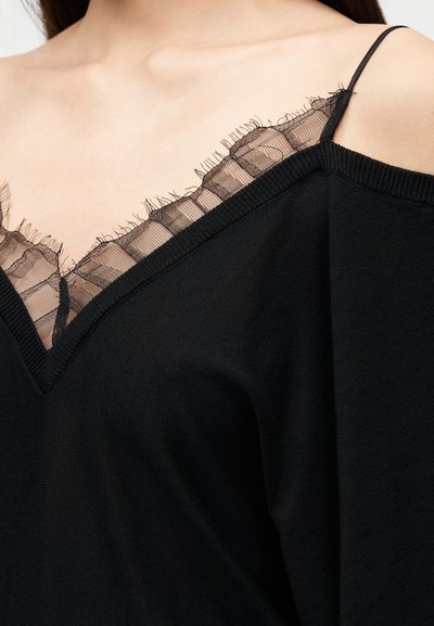 Haut noir avec un décolleté en V et une bordure en dentelle transparente. Il pr ésente de fines bretelles et un tissu doux et texturé. La dentelle a des bords effilochés.