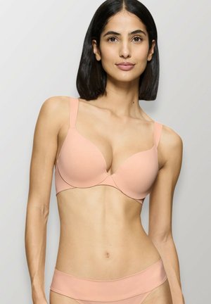 Reggiseno imbottito nudo con spalline regolabili e texture liscia. Design semplice, coppe sagomate e cucitura centrale per il supporto.
