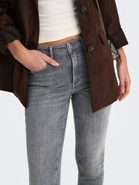 Brown suede coat over a white top, with mid-rise gray jeans featuring a classic five-pocket design and subtle fading.