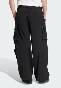 Černé pracovní kalhoty s volným střihem, vybavené několika bočními kapsami, elastickým pasem a hladkou, lehkou látkou.