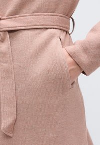 Παλτό από υφή υφασμάτινο ύφασμα σε ανοιχτό ροζ χρώμα, με ζώνη δετή, πλαϊνή τσέπη και μακριά μανίκια με λεία υφή.