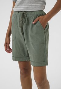 Shorts verts et légers avec une taille à cordon, jupes roulées, poches latérales et une finition en tissu texturé.