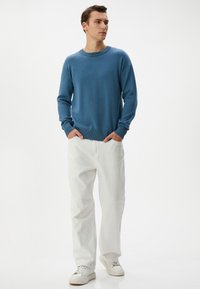 Hellblauer Strickpullover mit gerippten Bündchen und Saum, kombiniert mit off-white geraden Hosen und weißen Sneakers. Minimalistisches Design, weicher Stoff.