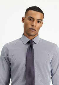Camisa de botón a rayas en azul claro y blanco, con cuello puntiagudo, acompañada de una corbata oscura con estampado. Textura de tela suave.