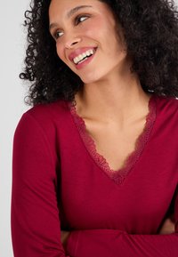 Bordeaux langemouwtop met een V-hals en kantafwerking. Zachte stof met een gladde textuur en een aansluitende silhoutte.