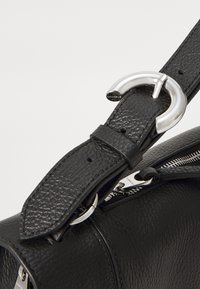 Black textured leather bag strap with silver rounded buckle and a visible silver zipper pull on a black leather bag.