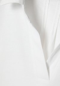 Witte katoenen shirt met een V-hals ontwerp, een gladde textuur en schone naden, die een minimalistische stijl uitstraalt.