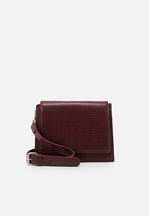 Sac à épaule bordeaux texturé avec une bandoulière amovible, présentant un design structuré et une forme rectangulaire, agrémenté de détails subtils en métal.