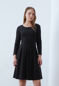Black long-sleeve dress with a fitted bodice and flared, pleated skirt. Smooth cotton fabric; classic round neckline and simple design.