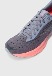 Scarpa da corsa violacea con tomaia in mesh perforato, dettagli blu chiaro e intersuola rosa, caratterizzata da una finitura testurizzata e lacci piatti.