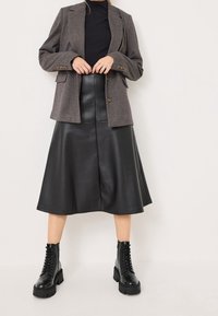 Šedý texturovaný blazer s hnědými knoflíky, kombinovaný s černou koženou midi sukni a černými šněrovacími bojovými botami.