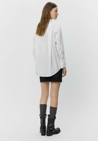 White long-sleeve shirt featuring a curved hem, paired with a black denim skirt and knee-high gray socks, complemented by black leather boots.