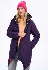 Fialový prošívaný kabát s květinovou podšívkou, se zipem, bočními kapsami a růžovou čepicí. Neformální vrstvení s broskvovou halenkou.