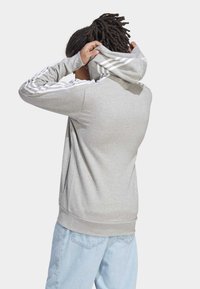 Felpa con cappuccio grigia in materiale morbido con strisce bianche lungo le maniche, cappuccio regolabile, tasca a marsupio e orlo a coste. Vestibilità casual.