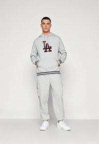 Siva jopa s kapuco z logotipom LA, prugastimi manšetami in ujemajočimi se hlačami s žeparji. Ima sprednji žep in bele superge. Preprost, priložnostni dizajn.