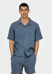 Blauwe kortekraag shirt met korte mouwen en bijpassende shorts van een gestructureerde stof met een subtiel ruitpatroon, voorzien van een kraag en een knopenlijst aan de voorkant.
