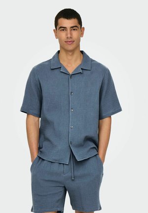 Camicetta blu a maniche corte e pantaloni assortiti realizzati in tessuto testurizzato con un sottile motivo a griglia, dotata di collo e bottoni frontali.