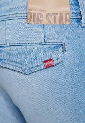 Jasnoniebieskie dżinsy z denimu z skórzaną naszywką z napisem "BIG STAR" oraz małą czerwoną metką na tylnej kieszeni. Prosty, teksturowany materiał.