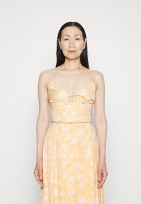 Vestido com padrão floral em amarelo claro, apresentando alças finas, um decote em V com um detalhe de laço no busto e uma saia fluida.