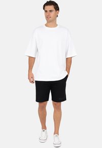 Witte oversized korte mouw T-shirt gecombineerd met zwarte shorts. Materiaal lijkt katoen te zijn, met een eenvoudig ontwerp. Schoeisel: witte sneakers.