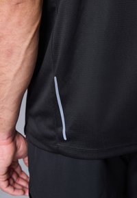 Črna atletska majica z texturirano površino, z ozkim sivim poudarkom ob stranskem šivu. Prikaz robov in območja rokava.