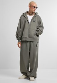 Gray zip-up hoodie and matching sweatpants made of soft fabric. Hooded design features "K" logo on the left chest and pant leg.