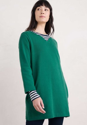 Groene tuniek met een V-hals, lange mouwen en zijzakken. Daaronder is een gestreept blauw-wit shirt zichtbaar bij de manchetten. Zachte stof, relaxte pasvorm.