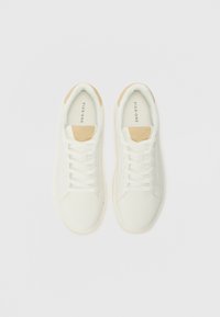 Baskets blanches avec une tige en cuir lisse, des accents en suède beige au talon et des lacets plats blancs. Semelle en caoutchouc avec des éléments de design minimaux.