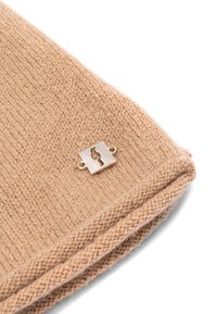 Beżowa dzianina o teksturowym wykończeniu, z małym kwadratowym złotym akcentem sprzętu z wyciętym wzorem.