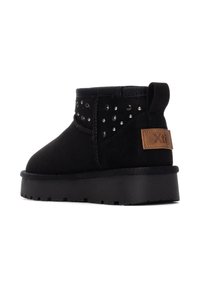 Botines de ante negro con acentos de tachuelas, superficie plana de goma y una etiqueta de cuero. Presenta una forma redondeada y un collar acolchado.
