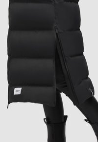 Schwarze gepolsterte Weste mit hohem Kragen, seitlichem Reißverschluss und Logopatch am Saum. Das Material ist glatt und hat eine glänzende Oberfläche.