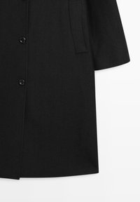 Cappotto nero in tessuto liscio, caratterizzato da un taglio dritto, una fila singola di bottoni e una tasca laterale. Design semplice senza motivi.