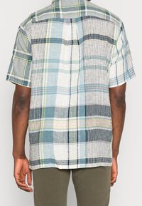Camicia a maniche corte a quadri con una combinazione di motivi blu, bianchi, verdi e neri, caratterizzata da texture differenti e un design del colletto standard.