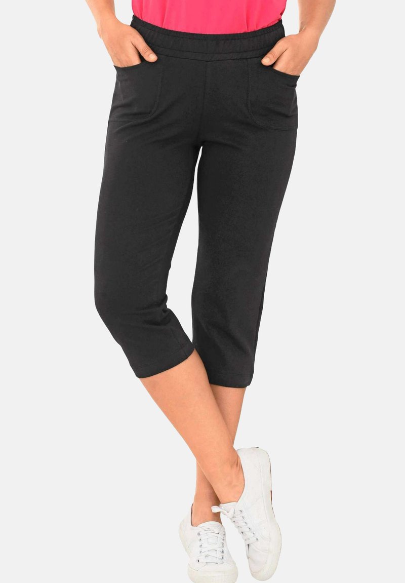 Zwarte capri-broek met een rekbare tailleband, twee zijzakken en een gladde textuur, gecombineerd met witte sneakers.