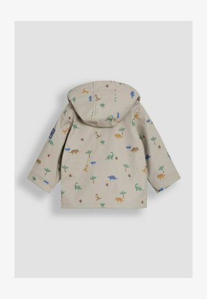 Šviesiai ruda striukė su kapišonu, puošta žaismingu dinozauro raštu žalia, mėlyna, oranžine ir ruda spalvomis, supamu mažų augalų.