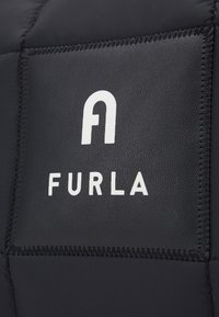 Czarna, pikowana faktura z wyraźnie wyeksponowanym białym logo "FURLA". Materiał wydaje się gładki, z kontrastującymi detalami przeszycia.