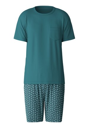 T-shirt corta color turchese con taschino sul petto abbinata a pantaloni corti a fantasia con cerchi concentrici bianchi e turchesi chiari su sfondo scuro.