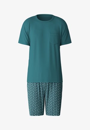 T-shirt corta color turchese con taschino sul petto abbinata a pantaloni corti a fantasia con cerchi concentrici bianchi e turchesi chiari su sfondo scuro.